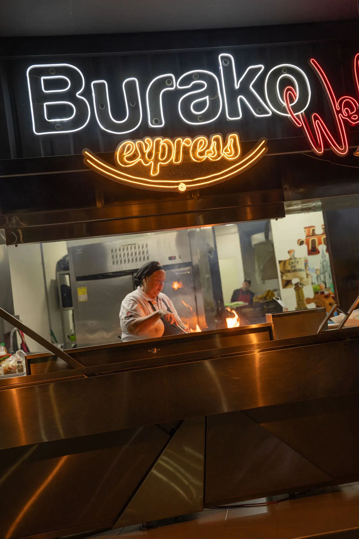 Estación de wok con letrero de neón Burako Express, cocinando entre llamas