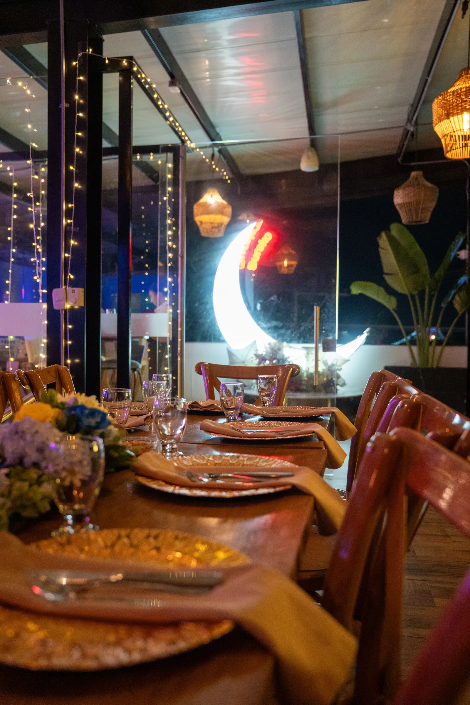 Terraza principal de Burako Gourmet de noche, mesas dispuestas junto a la luna de neón